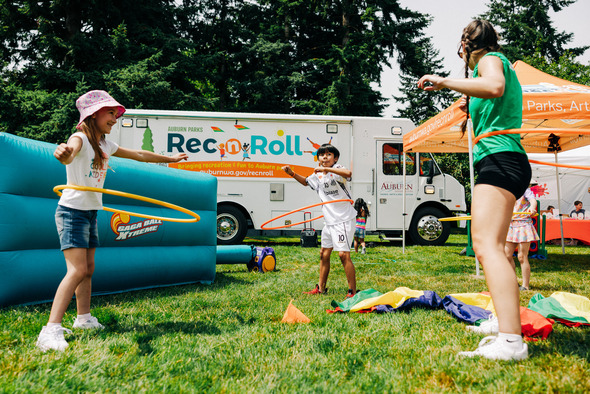Children playing with hula hoops in front of Auburn Parks' Rec n Roll truck at a sunny outdoor event.