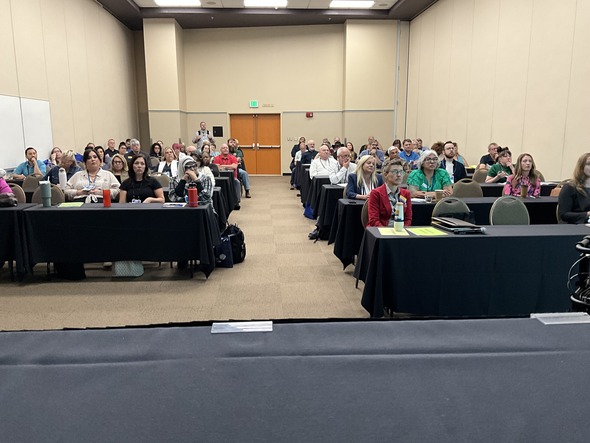 Audience attentively listens during a packed conference session in a large meeting room.