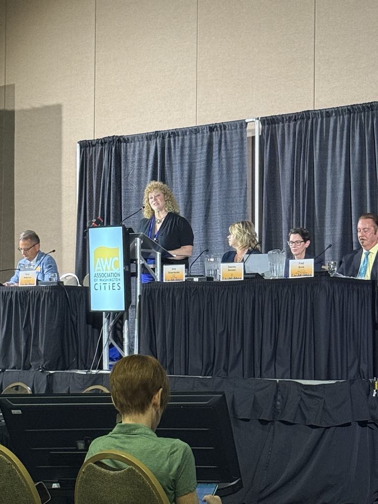 Panelists speak on stage at an Association of Washington Cities event with branding on the podium.