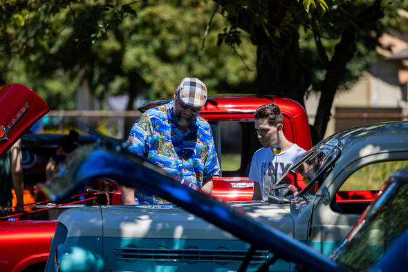 Two people admire the engine of a vintage truck at a classic car show on a sunny day.