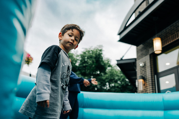 A young boy stands in a blue inflatable play area, looking curiously at the camera during an outdoor event.