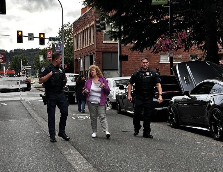 Three people walking down the road in Auburn with cars behind them 