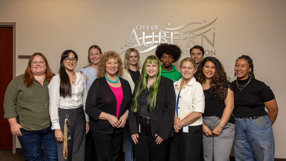 Mayor with a group of youth interns standing in front of City of Auburn logo.