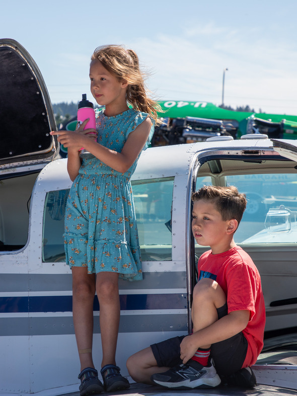 Girl and boy sit on a small aircraft wing, girl holding a pink water bottle.