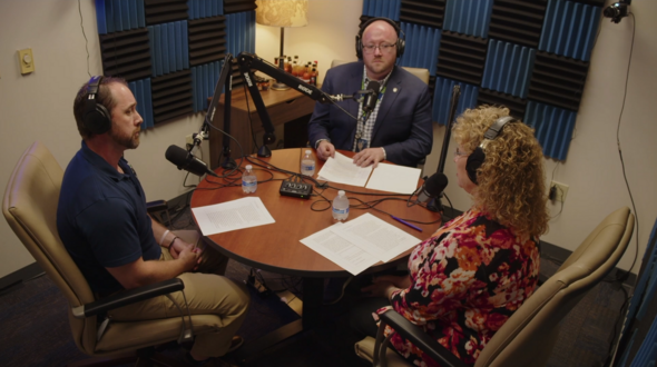 Mayor Backus and two guests record a podcast in a soundproof studio with microphones and notes on the table.