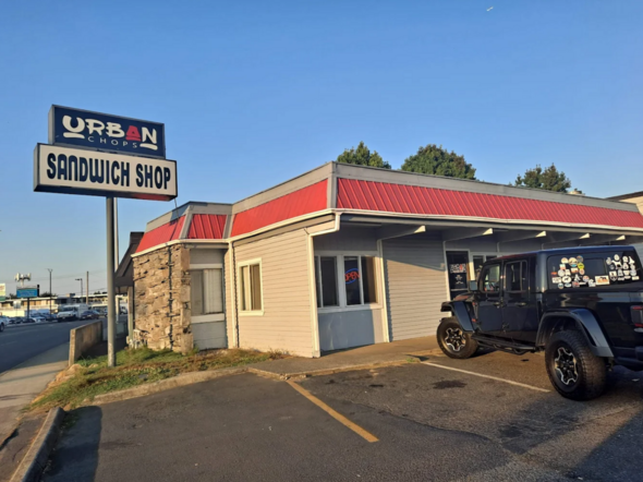 Exterior of Urban Chops Sandwich Shop with sign and parked Jeep under clear sky.