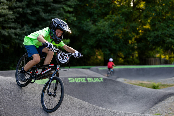 Youth in a neon green shirt racing a BMX bike on a pump track.