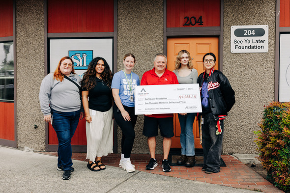 A group of people stand in front of a business holding a large check denoting over $1,000 was donated to a local nonprofit. 