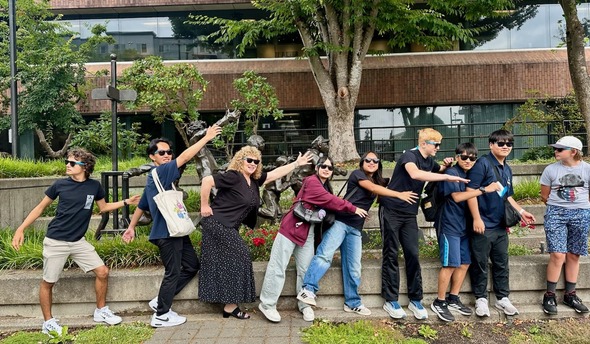 Group of people posing playfully in a line outdoors, each pointing in the same direction.