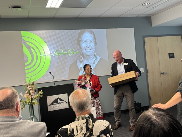Virginia Cross stands with flowers as a man presents a gift box during the award ceremony at Green River College.