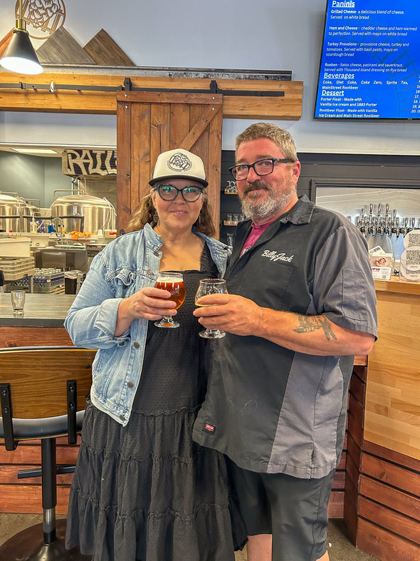 Couple holding beers inside a brewery, smiling at the camera.