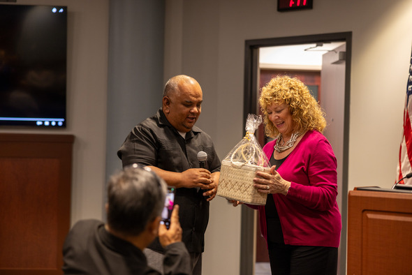 Man presents a gift basket to smiling woman during a city hall event.