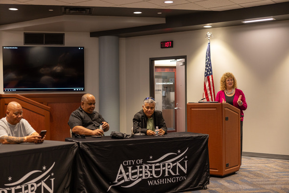 Woman speaking at a podium with “City of Auburn” banners and seated panelists nearby.
