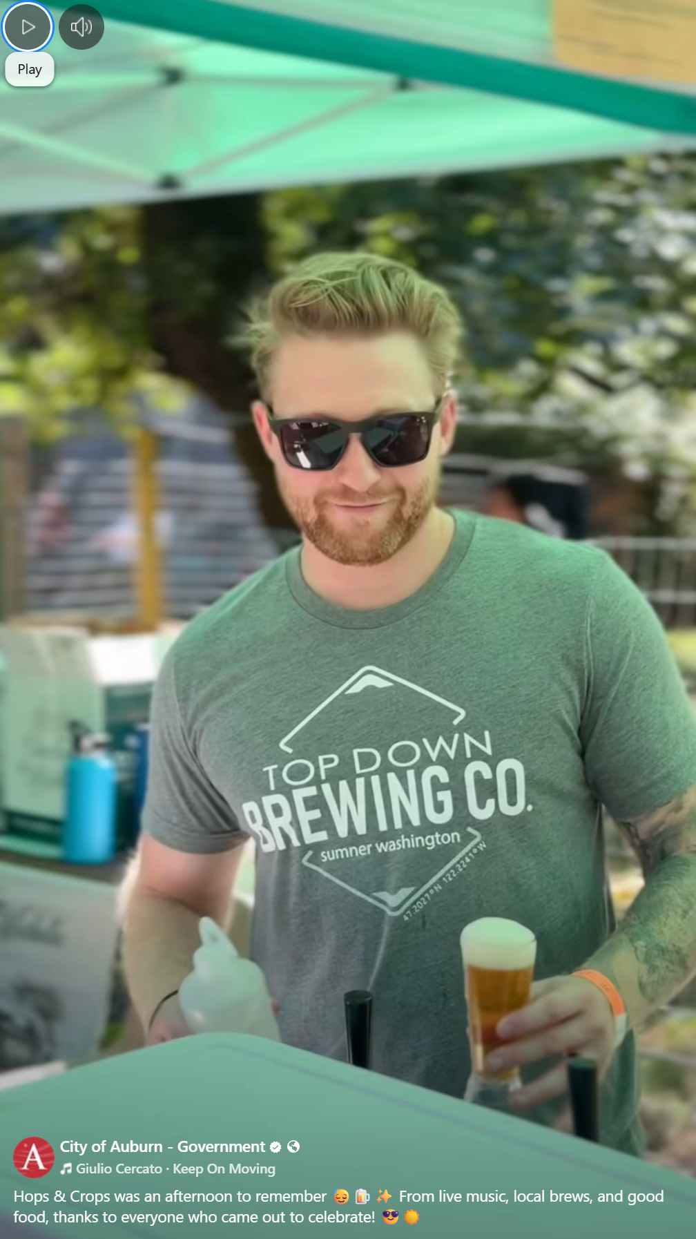 Man in sunglasses and Top Down Brewing Co. shirt serving beer at an outdoor event booth.