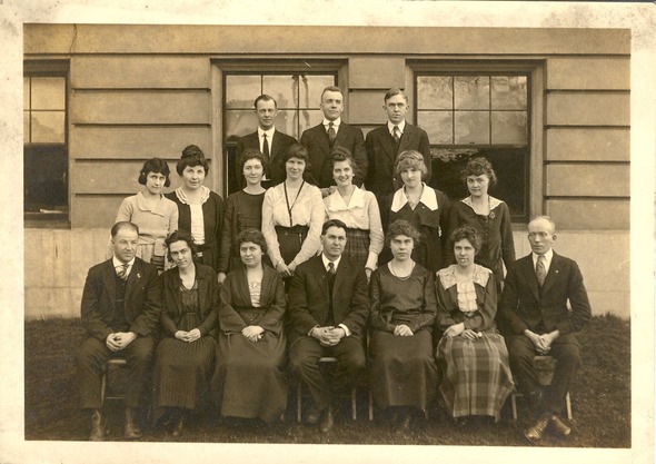 Black and white group portrait of men and women posing in front of a building.