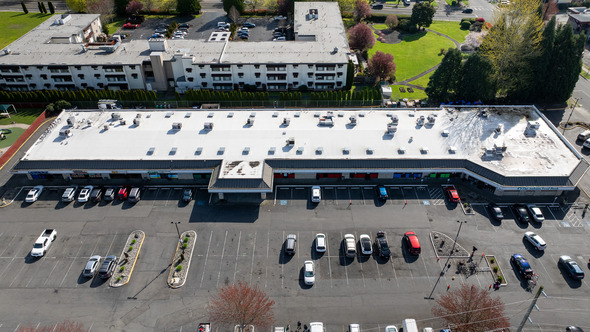 Aerial view of a strip mall with parked cars and apartment buildings behind it.