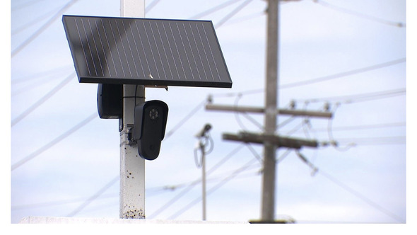 Close-up of a pole-mounted solar-powered camera with power lines in the background.