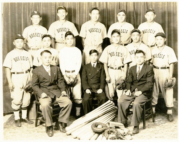 Black and white photo of the Bussei’s baseball team with players in uniform and three men in suits seated.