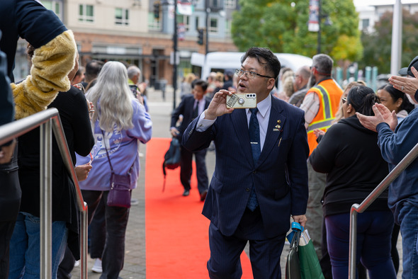 A suited man takes a photo of the crowd while walking the red carpet at the Auburn event.