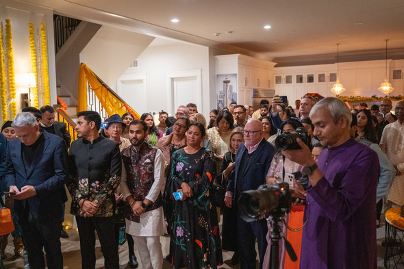 Large group listening to a speaker at an indoor Diwali celebration with colorful decor.