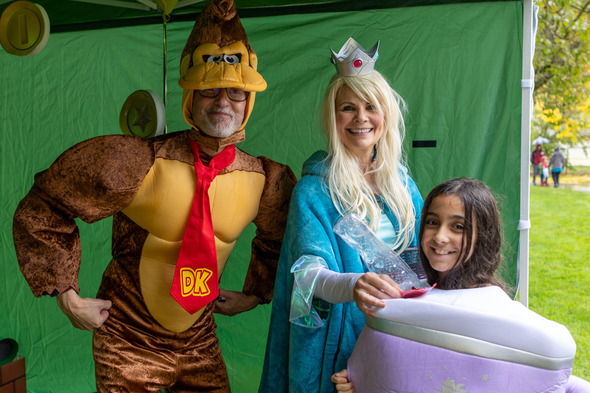 Two adults in Donkey Kong and princess costumes with a child dressed as cake at outdoor event.