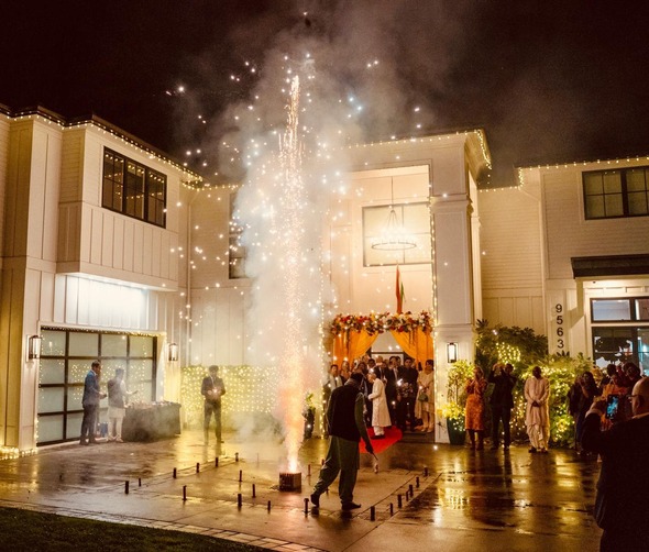 People celebrating Diwali outside a decorated house with fireworks and festive lights.