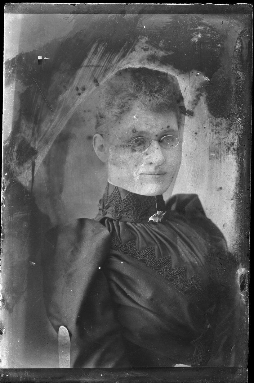Vintage black-and-white portrait of a woman in a high-collared dress and round glasses.