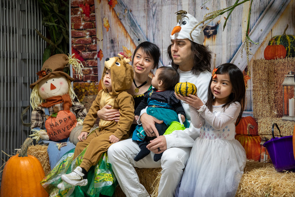 Family dressed as Frozen and Lion King characters pose with pumpkins in a fall-themed photo area.