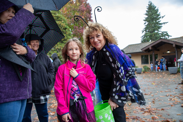 Mayor Nancy Backus, dressed as a butterfly, smiles beside a child in a pink jacket at a rainy fall event.