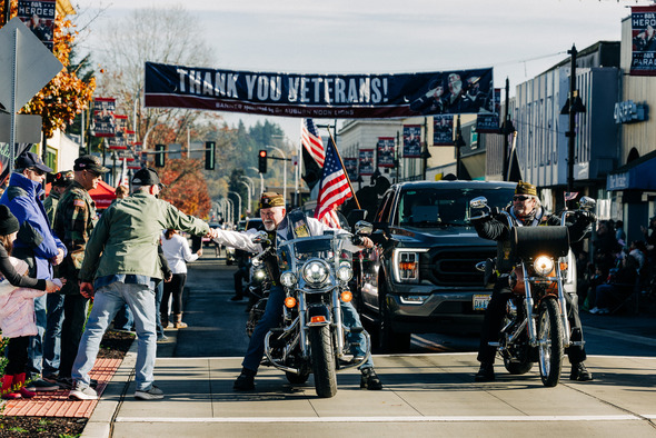 Motorcyclists in a Veterans Parade greet spectators under a “Thank You Veterans” banner.