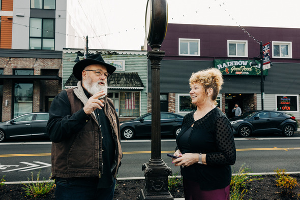 A man and woman talk beside the Auburn street clock with downtown storefronts behind them.
