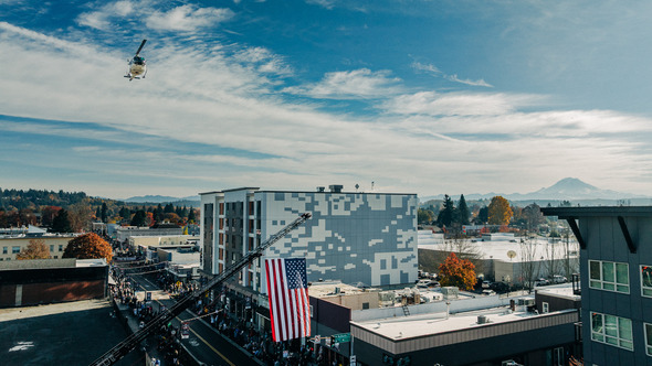 A helicopter flies above downtown Auburn as a giant American flag hangs from a ladder truck.