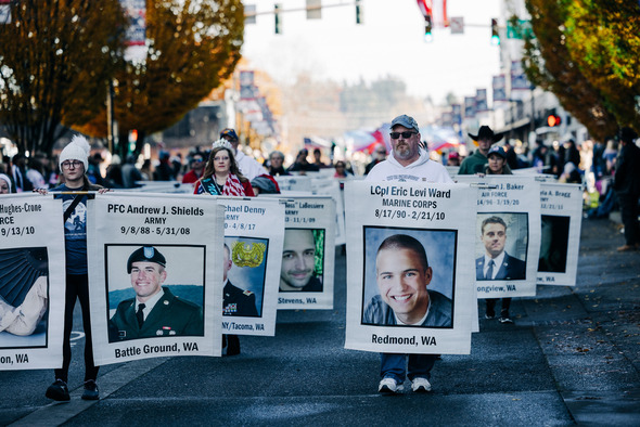 Parade participants carry large memorial banners honoring fallen service members.