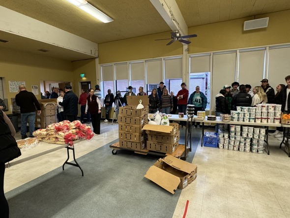 People lining up in a community room with tables full of bread, produce, and canned goods.