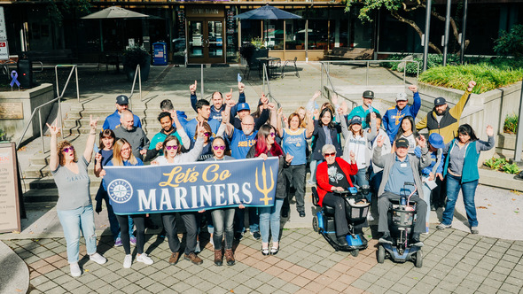 Large group outside City Hall holding a ‘Let’s Go Mariners’ banner and cheering.