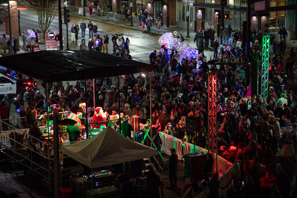 Large crowd gathers downtown around a lit stage during a nighttime holiday parade.