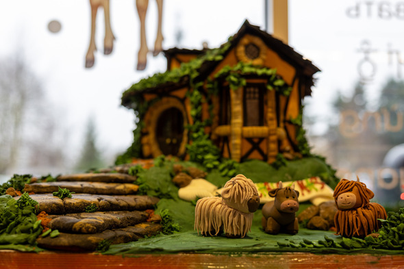 Detailed gingerbread scene with a cottage, stone path, and three small animal figures on green icing.