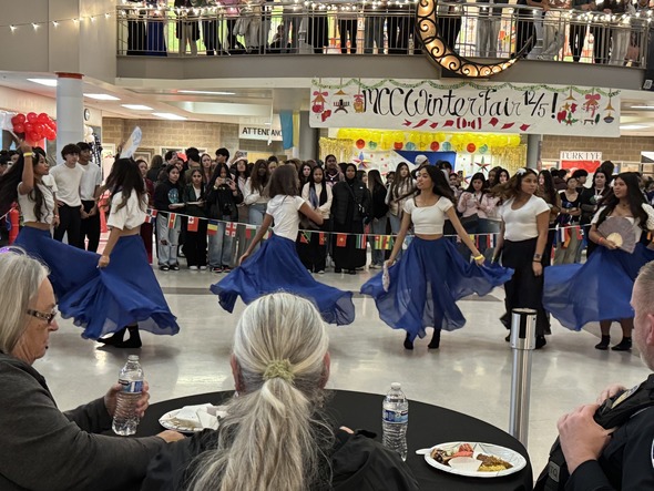 Dancers in white tops and flowing blue skirts perform while attendees watch during the MCCA Winter Fair.