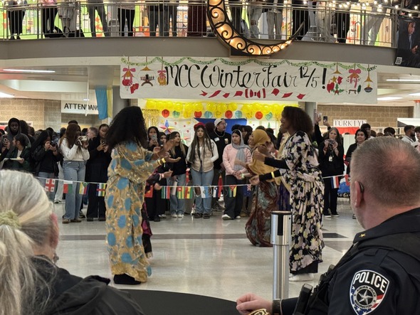 Students perform a cultural dance in colorful outfits as a large crowd watches at the MCCA Winter Fair.”