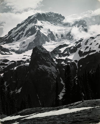 Snow-covered mountain peaks rising above rocky terrain and evergreen trees.