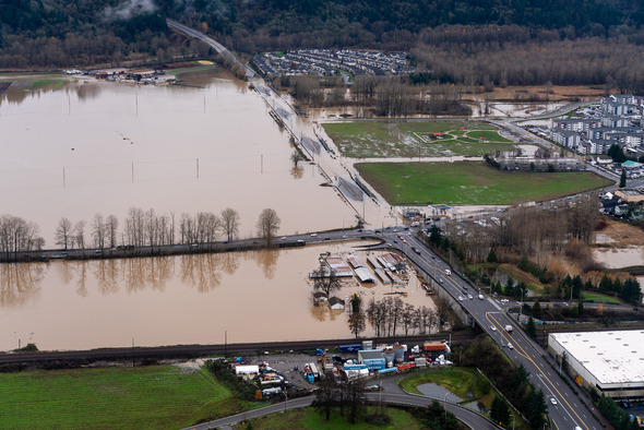 Aerial view of flooded fields and roads near a residential area following heavy rain.