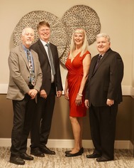 Four people standing in a room with a beige background 