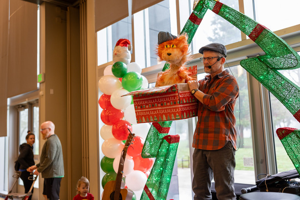 A man on a stage holding a present box with a puppet cat popping out of it 