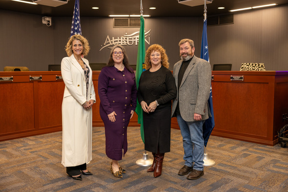 Four newly sworn-in Auburn elected officials pose together in council chambers with city flags behind them.
