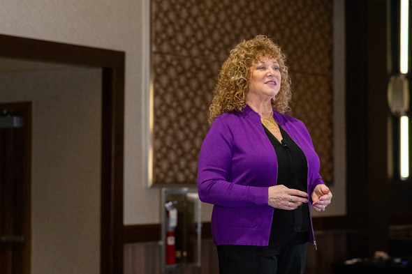 Auburn Mayor speaks to an audience indoors, wearing a purple cardigan and microphone, mid-speech.