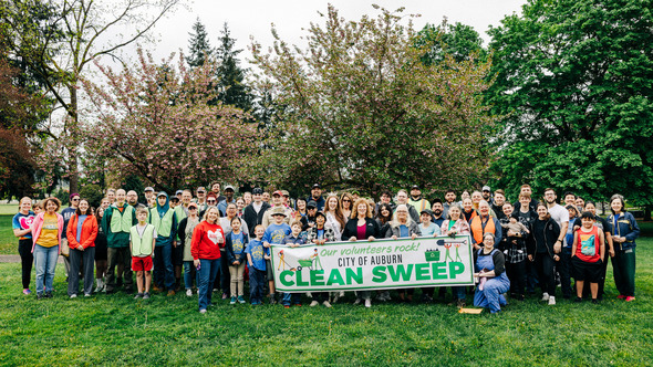 Large group of volunteers gathered in a park holding a “City of Auburn Clean Sweep” banner.