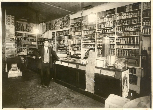 A man standing in an old grocery/pharmacy store. Photo is black and white 