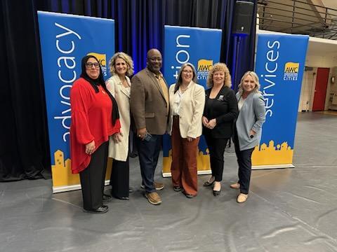 Group of seven attendees pose in front of AWC banners labeled Advocacy, Action, and Services at City Action Days.