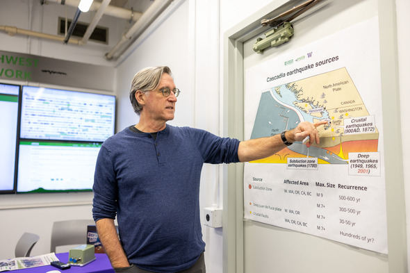 A man standing in a room pointing at a map 