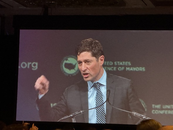 Speaker addressing the audience on a large screen at the U.S. Conference of Mayors conference.